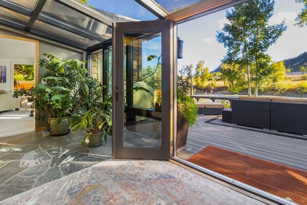 Un intérieur moderne avec une porte vitrée donnant sur une terrasse extérieure, des plantes en pot et une vue sur un paysage montagneux.