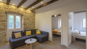 Un salon chaleureux avec un canapé d’angle gris, une table basse ronde et un mur en pierre.