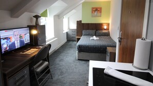 A hotel room with a bed, a desk with a computer, a chair, a window, and a door. - Victoria House - Deluxe Studio by CovStays (Coventry)