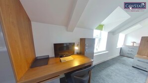 A modern, well-lit room with a wooden desk, a computer, and a chair. There is a window providing natural light and a view of the outside. - Victoria House - Deluxe Studio by CovStays (Coventry)