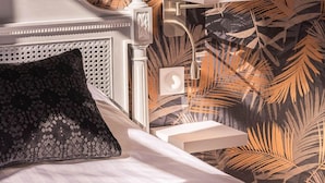 A bedroom with a bed, a nightstand, a lamp, and a wall with a tropical leaf pattern. - La Suite N°3 Appt n°IV Charming historic center of Avignon (Avignon)