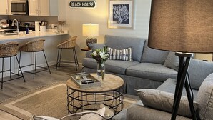 Una sala de estar moderna con un sofá, sillones, una mesa de centro y un comedor, con una cocina al fondo.