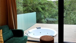 Una habitación moderna con un sofá verde, una mesa redonda y un amplio ventanal con vistas a un bosque.