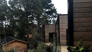 Un edificio moderno con fachada de madera, barandilla de vidrio y vistas a árboles y edificios circundantes.