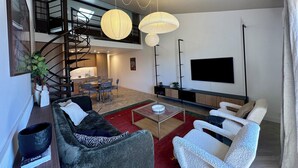 Un soggiorno moderno con una scala, un'area pranzo e una televisione a schermo piatto montata a parete.