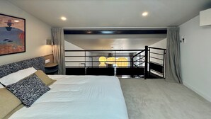 Una camera da letto con un letto, un quadro, una scala e vista su un balcone.