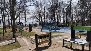 A playground with various equipment, including swings and a climbing structure, surrounded by trees and a sandy area. - Three-room apartment with 2 bathrooms for up to 8 people. (Kellenhusen)