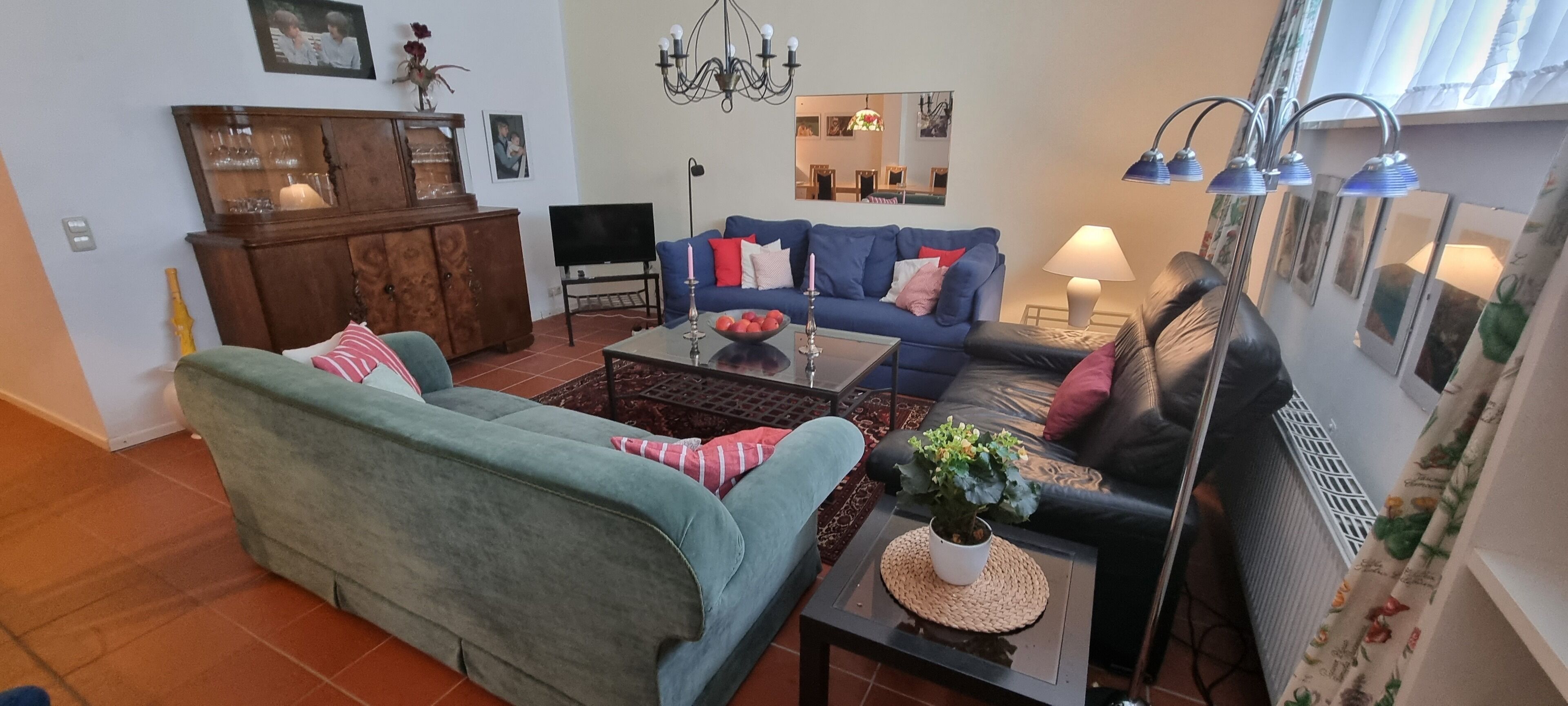 A living room with a blue sofa, a green sofa, a coffee table with a plant, a TV, and a wooden cabinet.