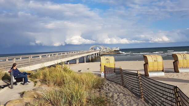 A coastal walkway with a wooden bench, a bridge, and beach huts. - Three-room apartment with 2 bathrooms for up to 8 people. (Kellenhusen)