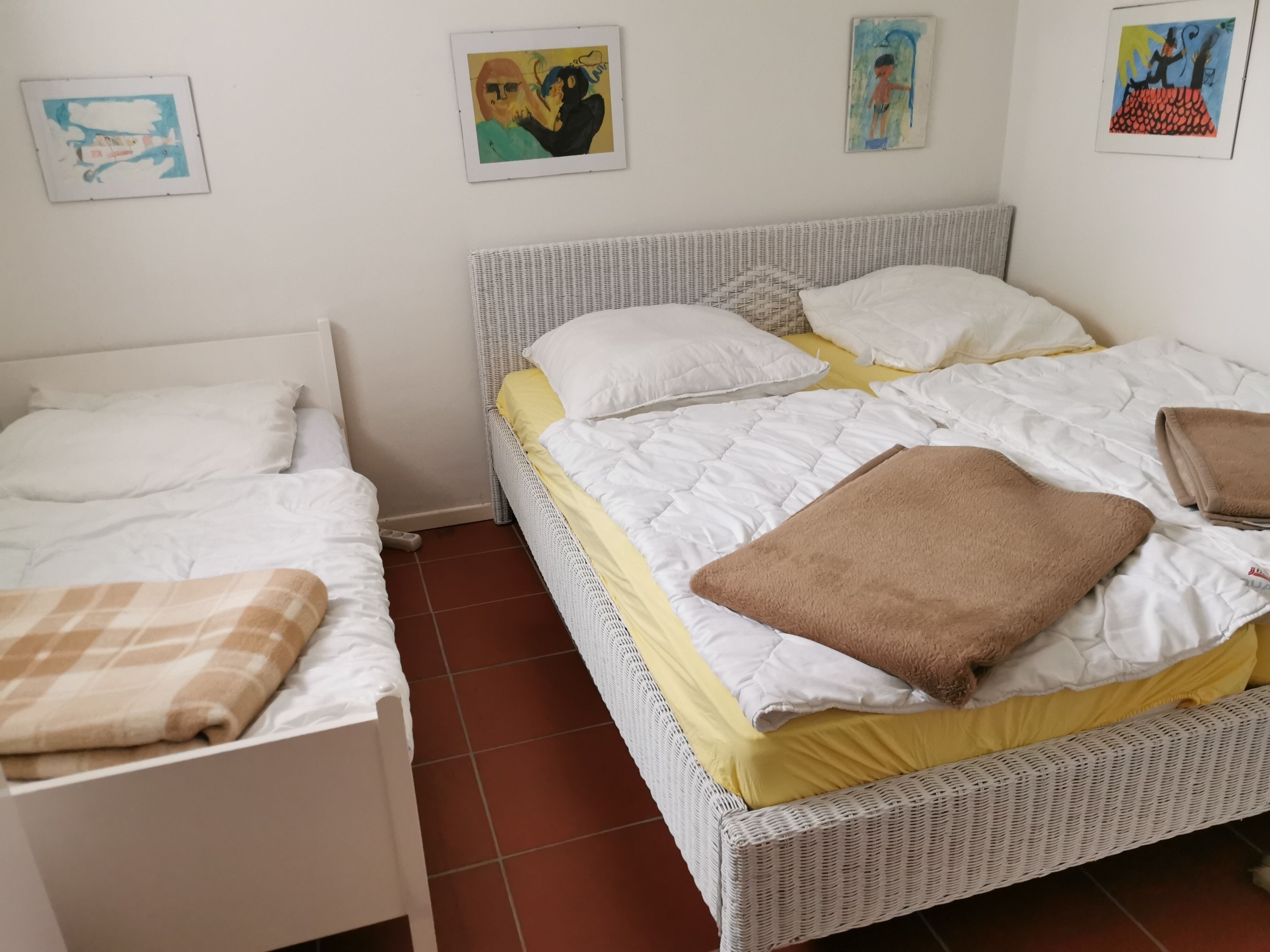 Ein Zimmer mit zwei Einzelbetten, einem Doppelbett und einem weißen Rattan-Kopfstück.