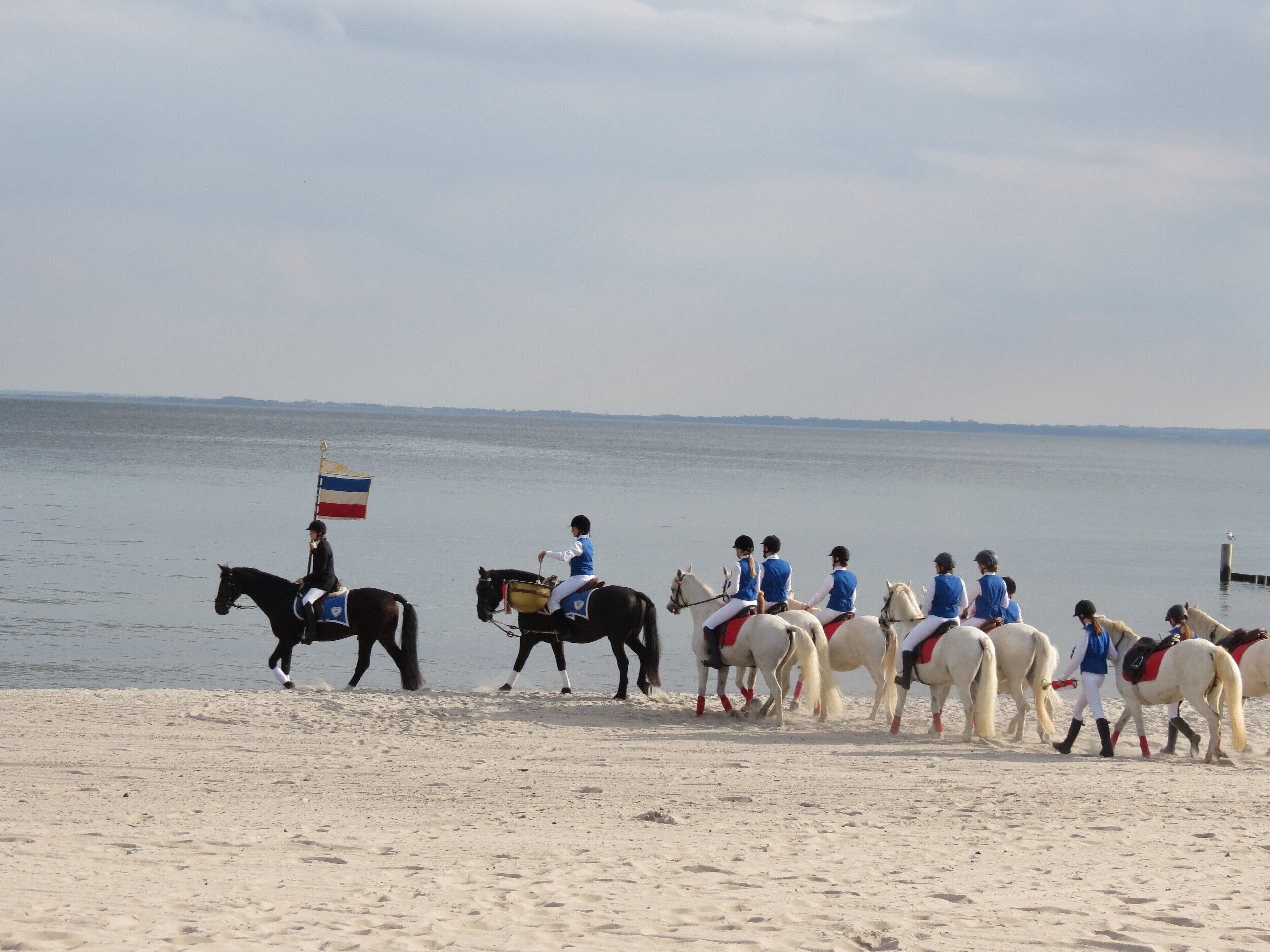 Une plage où l’on voit des chevaux et des cavaliers, dont certains brandissent des drapeaux.