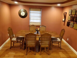 Enjoy meals in this dining room with a large table and four chairs, a decorative clock, and a window with blinds.
