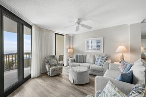 A spacious living room with a large window, a ceiling fan, and a view of the outdoors. - Seaside Paradise 3BR Condo Steps from the Beach (Pawleys Island)