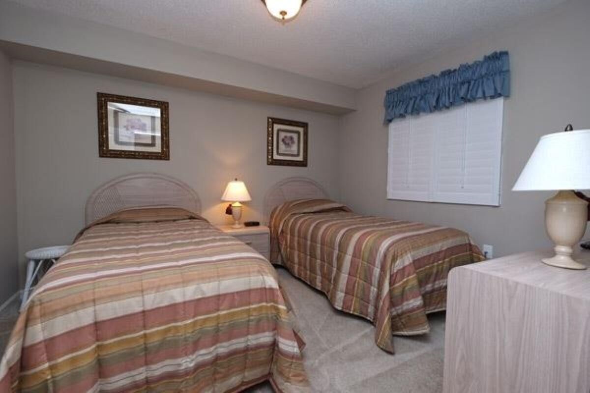 Una habitación con dos camas, cada una con ropa de cama a rayas, una mesita de noche con lámpara y cuadros enmarcados en la pared.