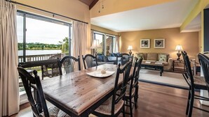 Un comedor con mesa y sillas de madera, un sofá y vistas a un jardín a través de ventanas grandes.