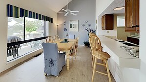 Comedor con mesa y sillas de madera, ventilador de techo y vistas amplias a través de grandes ventanales.