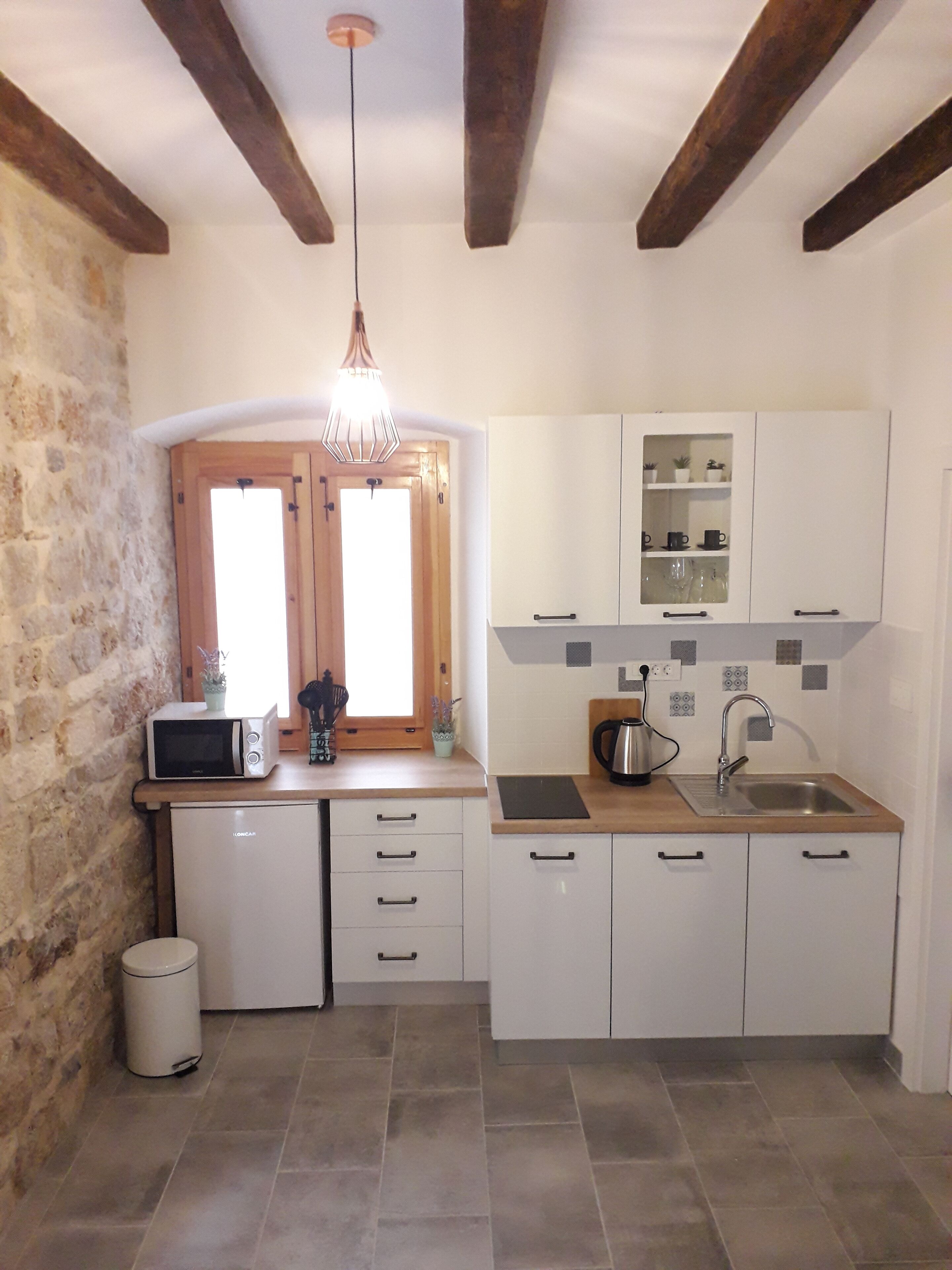 Una cocina compacta con armarios blancos, microondas, pileta y pared de piedra.