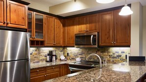 A kitchen with wooden cabinets, a stainless steel refrigerator, a microwave, granite countertops, and a stone backsplash. - Spacious (700 sqft) 1 Bedroom/1 Bath cozy Condo /Pool & Hot tubs (Canmore)