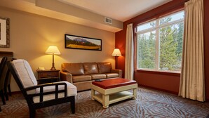 A hotel room with a leather sofa, a wooden armchair, a small table, and a large window with curtains. - Spacious (700 sqft) 1 Bedroom/1 Bath cozy Condo /Pool & Hot tubs (Canmore)