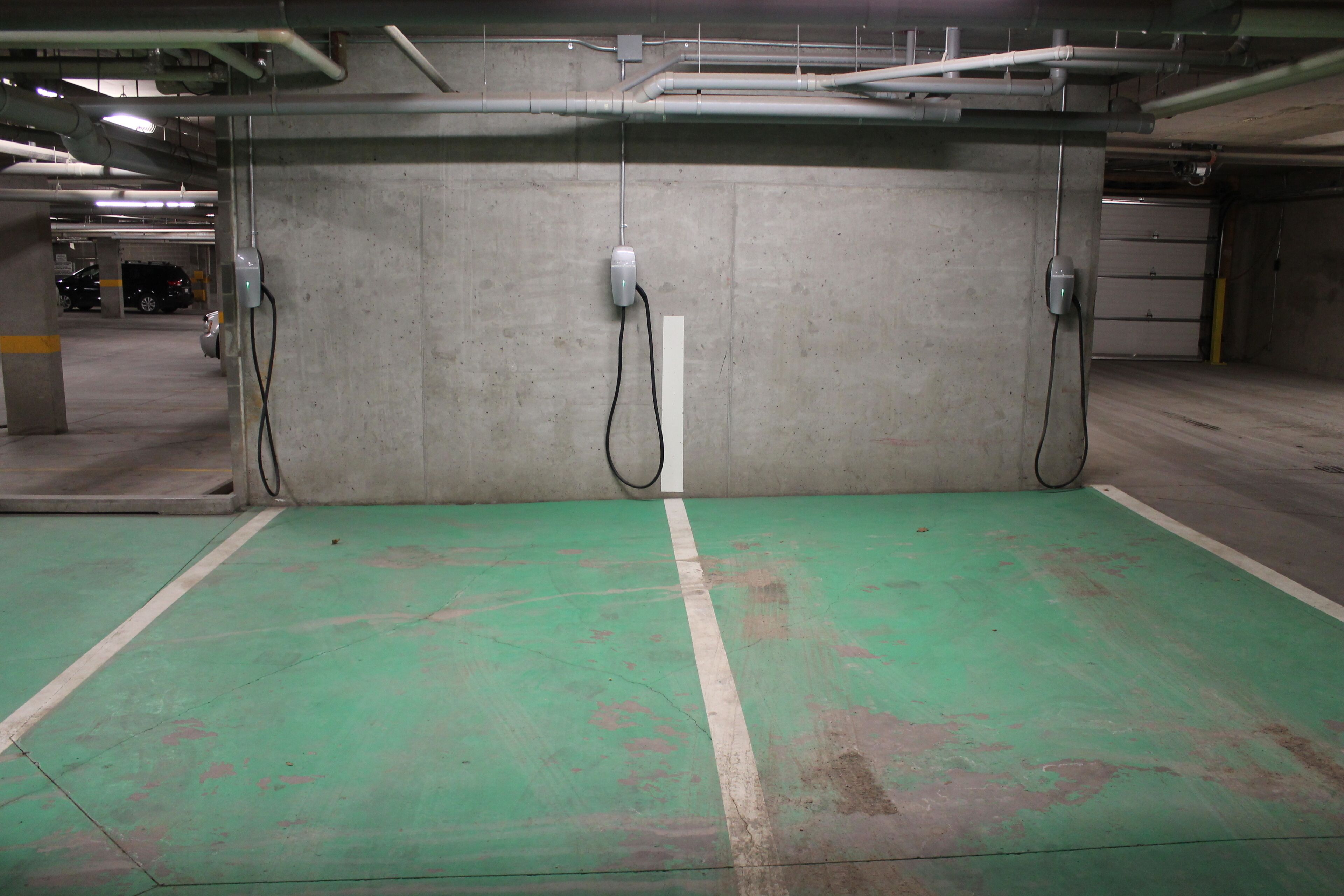 Un parking avec des murs en béton, des marquages verts au sol et des tuyaux apparents au plafond.