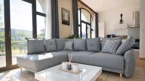 Una sala de estar moderna con un sofá seccional gris, una mesa de centro blanca y un ventanal que ofrece vistas al exterior.