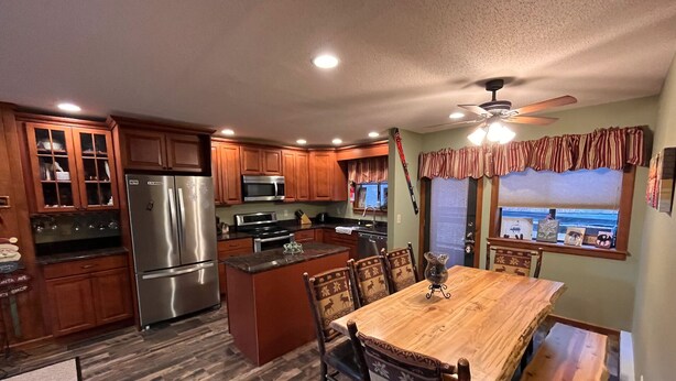 A kitchen with wooden cabinets, stainless steel appliances, and a dining area with a wooden table and chairs. - Cozy Killington Mountain View Condo (Killington)