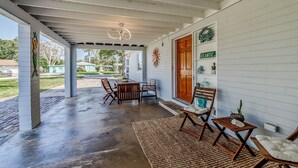 A covered porch with a wooden table and chairs, a rug, and a bench.