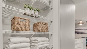 A neatly organized storage area with shelves holding folded towels, wicker baskets, and a laundry basket.