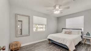 A bedroom with a bed, a ceiling fan, a large mirror, and a window.