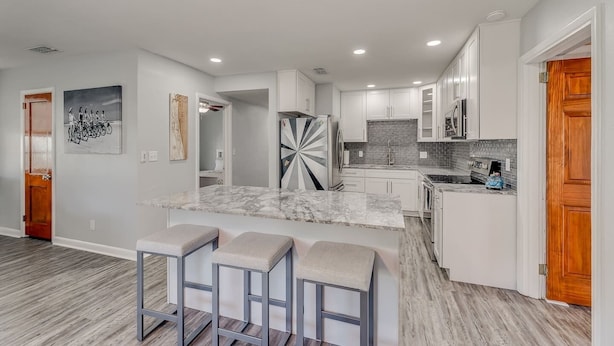 A modern kitchen with white cabinets, a marble countertop, and a built-in island with bar stools.