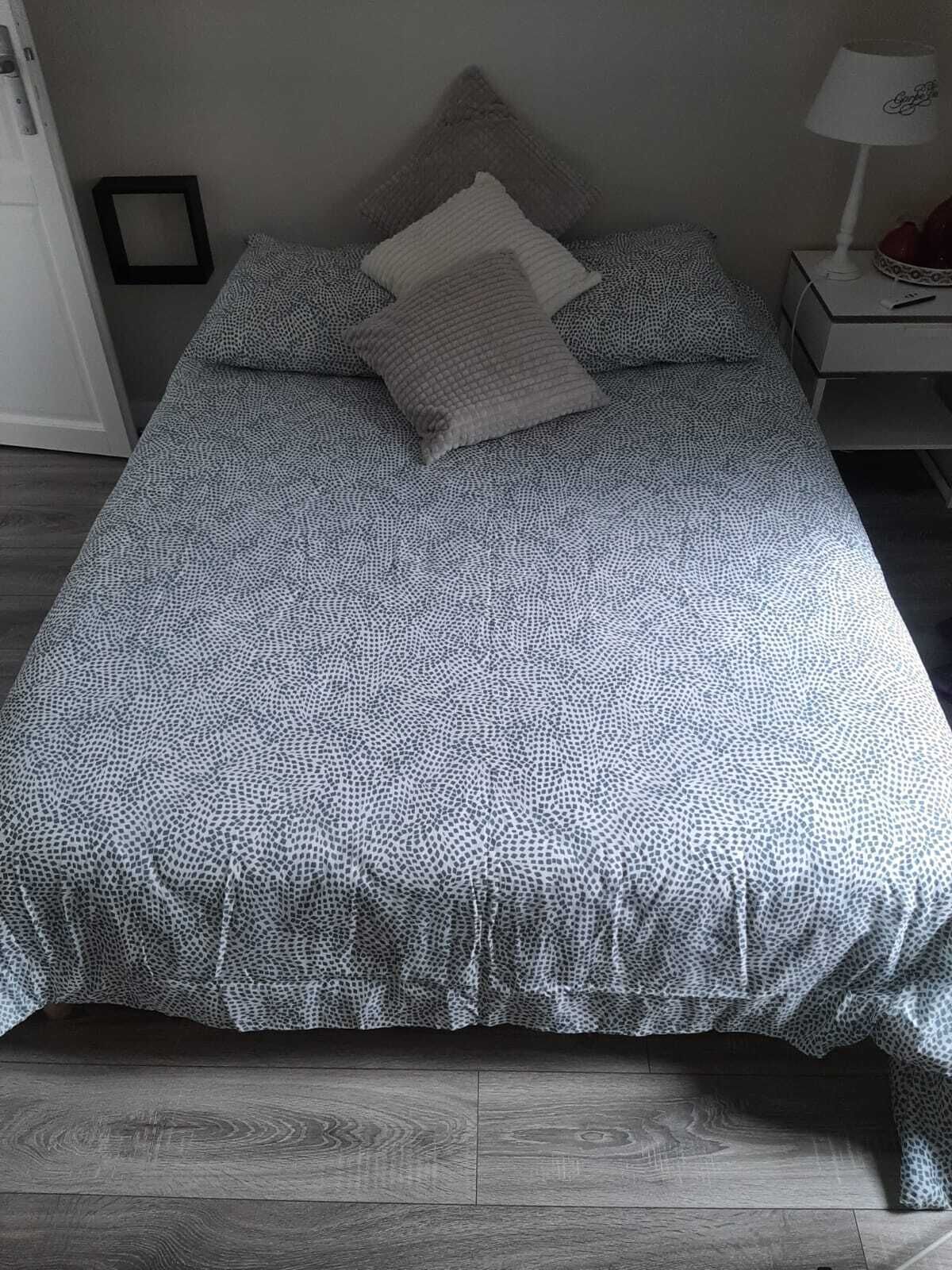 A bed with a patterned bedspread, pillows, and a bedside table with a lamp.