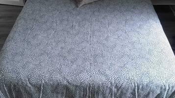 A bed with a patterned bedspread, pillows, and a bedside table with a lamp.