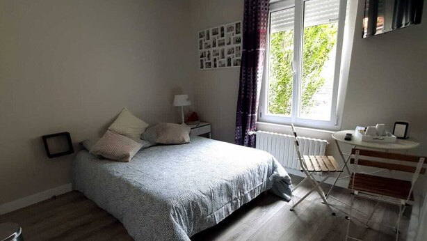 Ein Schlafzimmer mit einem Bett, einem Heizkörper, einem Fenster mit Vorhängen, einem Schreibtisch und einem Stuhl.