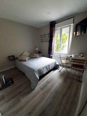A bedroom with a bed, a radiator, a window with curtains, a desk, and a chair. - Private apartment, 40 minutes from Paris (Mennecy)