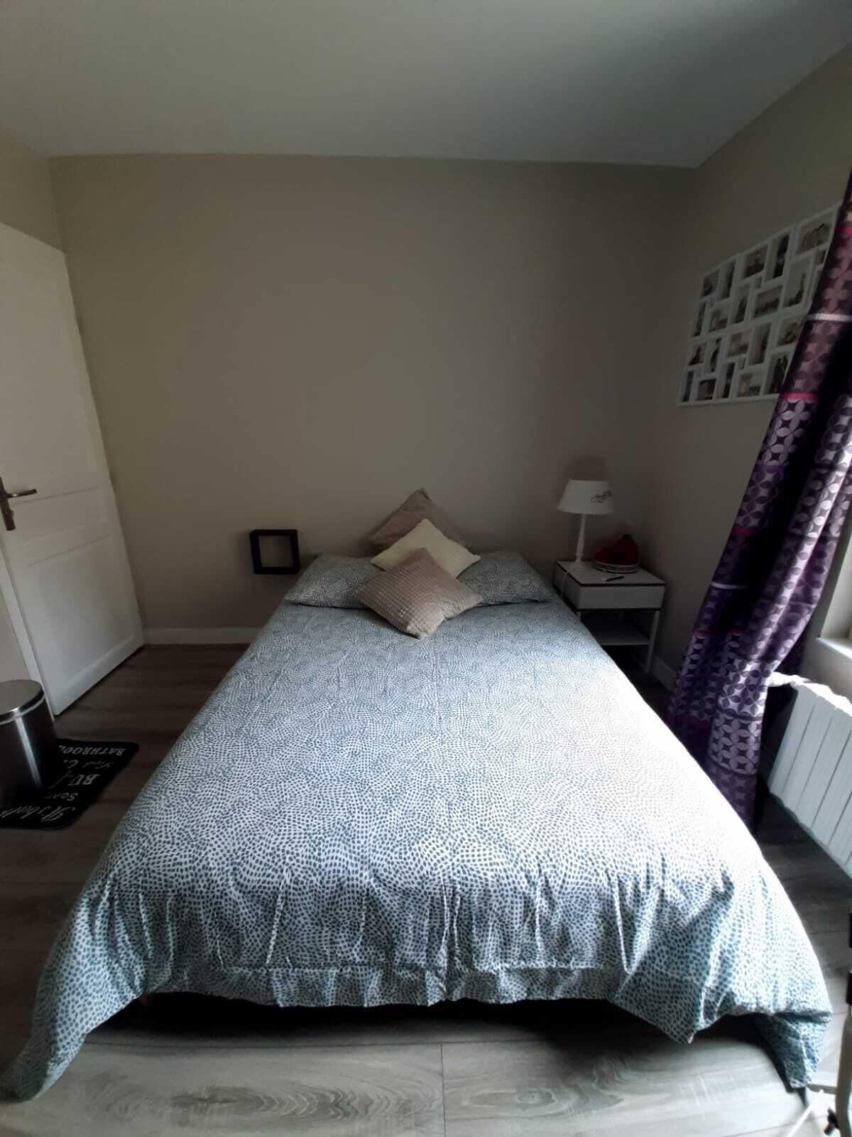 A bedroom with a bed, a nightstand, a lamp, a door, and a curtain.