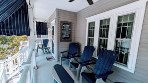 Une véranda couverte avec des fauteuils Adirondack et un banc, un panneau d’accueil et un ventilateur de plafond.