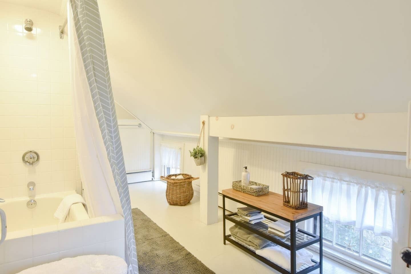 A modern bathroom with a bathtub, shower, and a window with curtains.