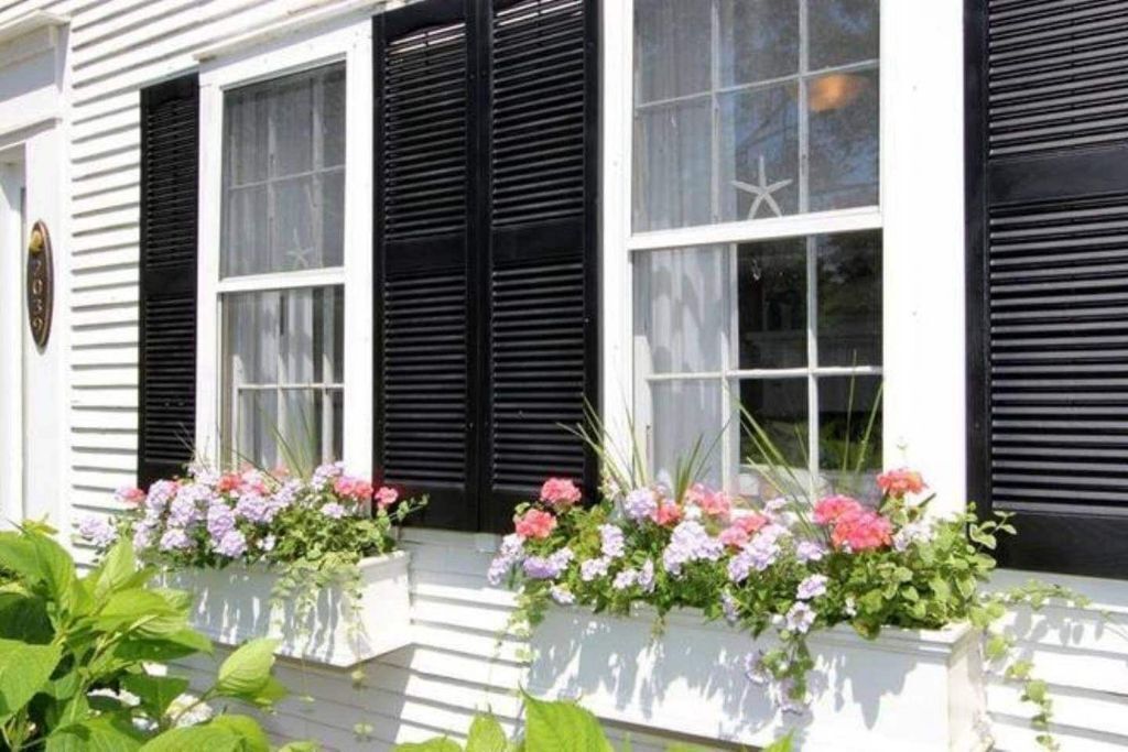 Un bâtiment blanc avec des volets noirs et des jardinières sur les rebords des fenêtres.