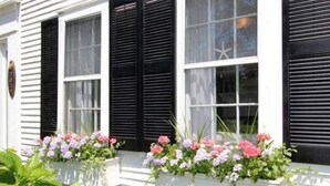 Un bâtiment blanc avec des volets noirs et des jardinières sur les rebords des fenêtres.