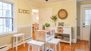 Une pièce chaleureuse avec un plancher en bois, des meubles blancs, un lustre et un mur décoré de différents objets.