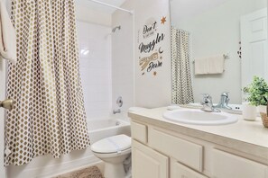 A bathroom with a white bathtub, a toilet, and a sink with a mirror. There is a towel rack and a potted plant on the sink counter.