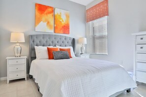 A modern bedroom with a large bed, two bedside tables with lamps, a grey upholstered headboard, and abstract wall art.