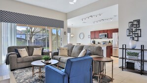 A modern living room with a sofa, chairs, and a coffee table. There is a kitchen in the background with cabinets and appliances.