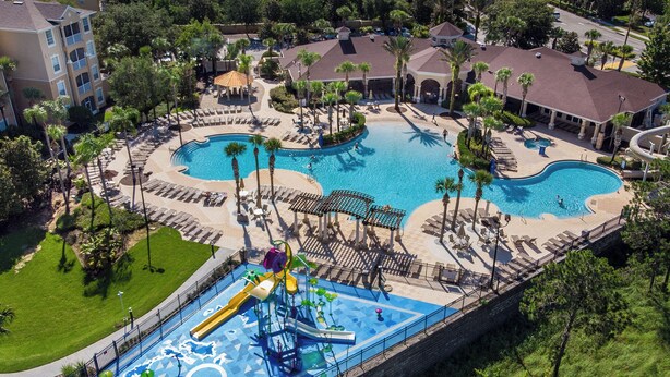 A resort with a large central pool, a water slide, and multiple lounge areas with umbrellas.
