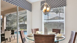 A dining area with wicker chairs, a glass table, and a chandelier.