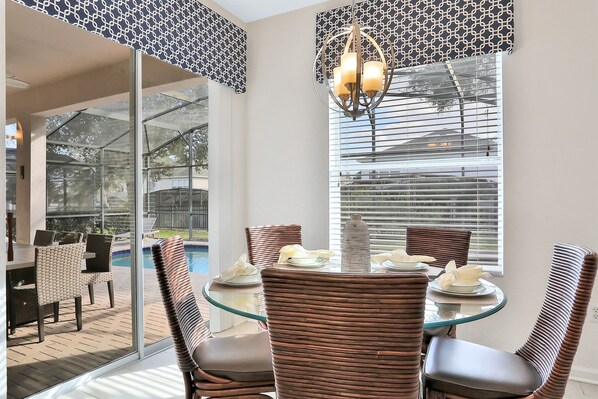 A dining area with wicker chairs, a glass table, and a chandelier.