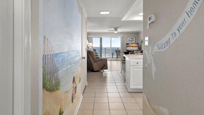 Un couloir décoré d’une fresque représentant une plage, avec un fauteuil inclinable, un téléviseur et une pancarte indiquant : « Bienvenue chez vous ».