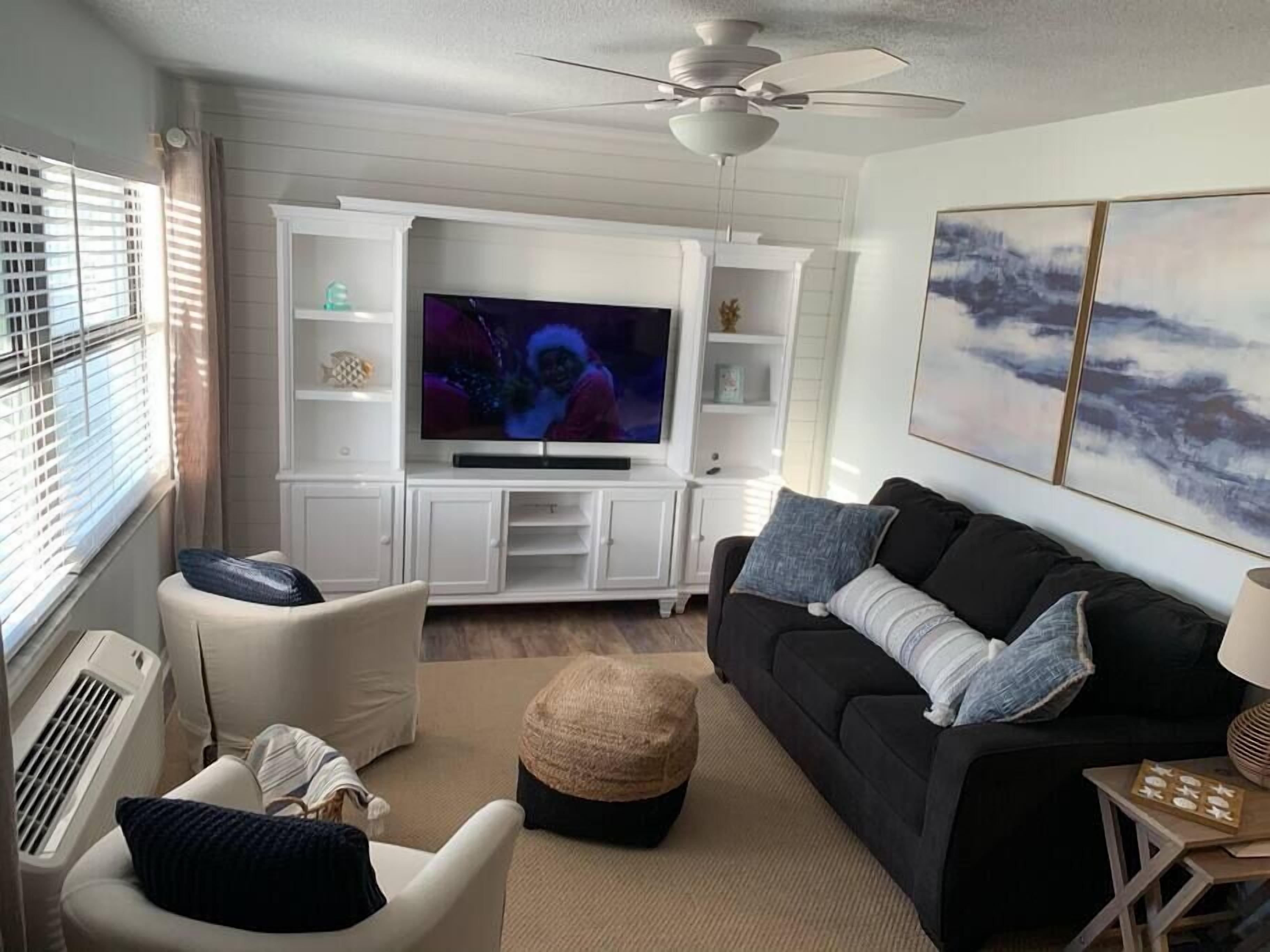 Ein Wohnzimmer mit Fernseher, weißen Schränken, einem schwarzen Sofa und einem Deckenventilator.