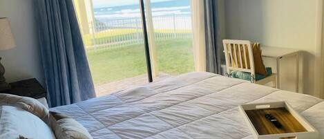 A bedroom with a large bed, a nightstand, a TV, and a view of the ocean through a sliding glass door.