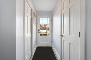 Corredor com portas brancas, um tapete de entrada preto e vista de um edifício através de uma porta de vidro.